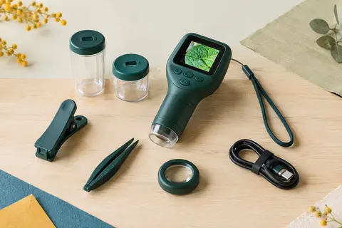 Kit numérique vert foncé pour observer les insectes, avec pince, gobelets, loupe et câble sur bois clair.