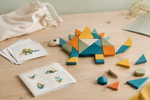 Puzzle géométrique en bois multicolore avec pièces assemblées, cartes défis et sac de rangement sur une table claire