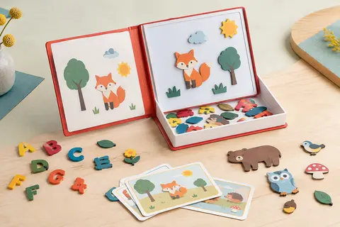 Magneti’Book rouge ouvert, avec ses lettres magnétiques et ses magnets illustrés posés sur un fond clair.