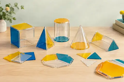 Solides géométriques transparents et formes pliables colorées disposés sur une table en bois clair.