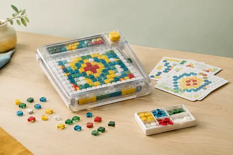 Jeu de mosaïque mécanique multicolore avec boîtier transparent, boutons et fiches de motifs sur une table claire.