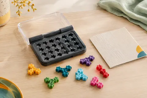 Plateau compact de jeu de logique avec sept pièces étoiles colorées sur une table en bois clair.