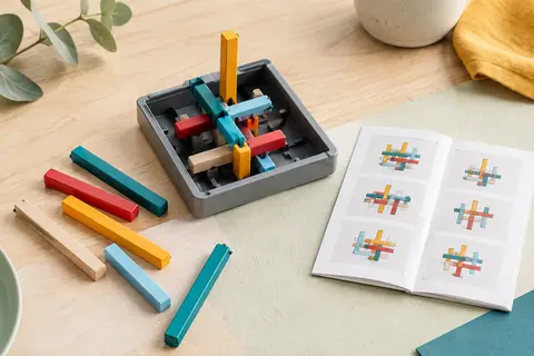 Plateau de jeu IQ Stixx avec ses bâtonnets colorés croisés et le livret de défis posé à côté.